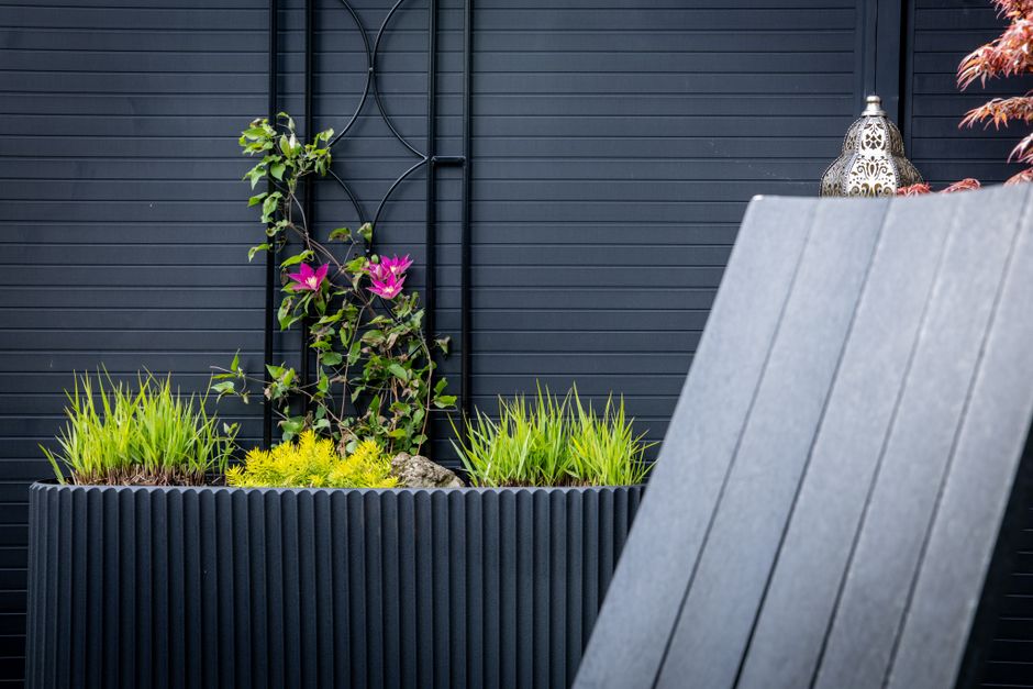 Moderne plantenbak zonder bodem in een groene tuin met bloeiende planten en cortenstaal.
